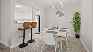 A modern kitchen with white cabinets, a stainless steel refrigerator, and a dining area with a wooden table and white chairs. - Family Friendly 2BR 2BA in the City (Rochester)