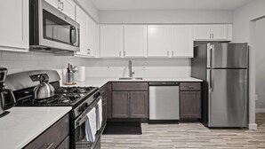A modern kitchen with white cabinets, stainless steel appliances, and a tiled floor. - Family Friendly 2BR 2BA in the City (Rochester)