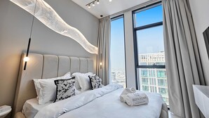 Ein modernes Hotelzimmer mit einem großen Bett, Blick auf die Stadt und einer außergewöhnlichen Deckenleuchte.