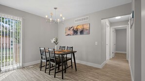 A dining area with a table and chairs, a chandelier, a painting on the wall, and a view through a sliding glass door. - Bright and Airy 2BR 2BA in the Heart of the City (Rochester)