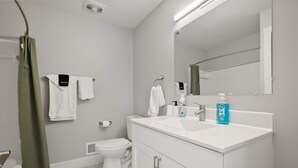 A modern bathroom with a white sink, two towel racks, a toilet, and a shower curtain. - Bright and Airy 2BR 2BA in the Heart of the City (Rochester)