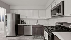 A modern kitchen with stainless steel appliances, dark wooden cabinets, and a white tiled backsplash. - Comfy 2BR 2BA Unit in Pime Location (Rochester)