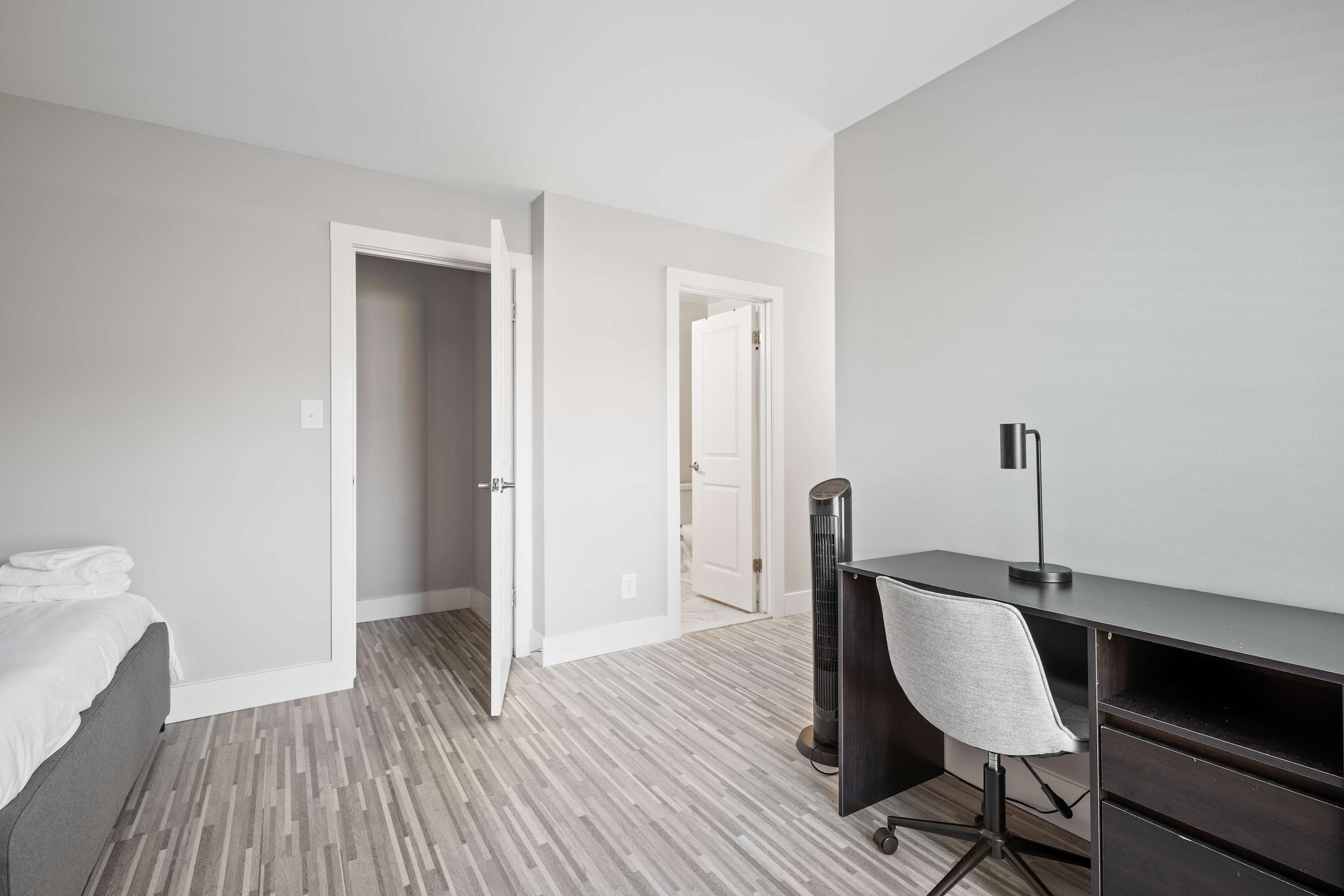 A bedroom with a bed, a desk, and a chair. There are two doors leading to other rooms.