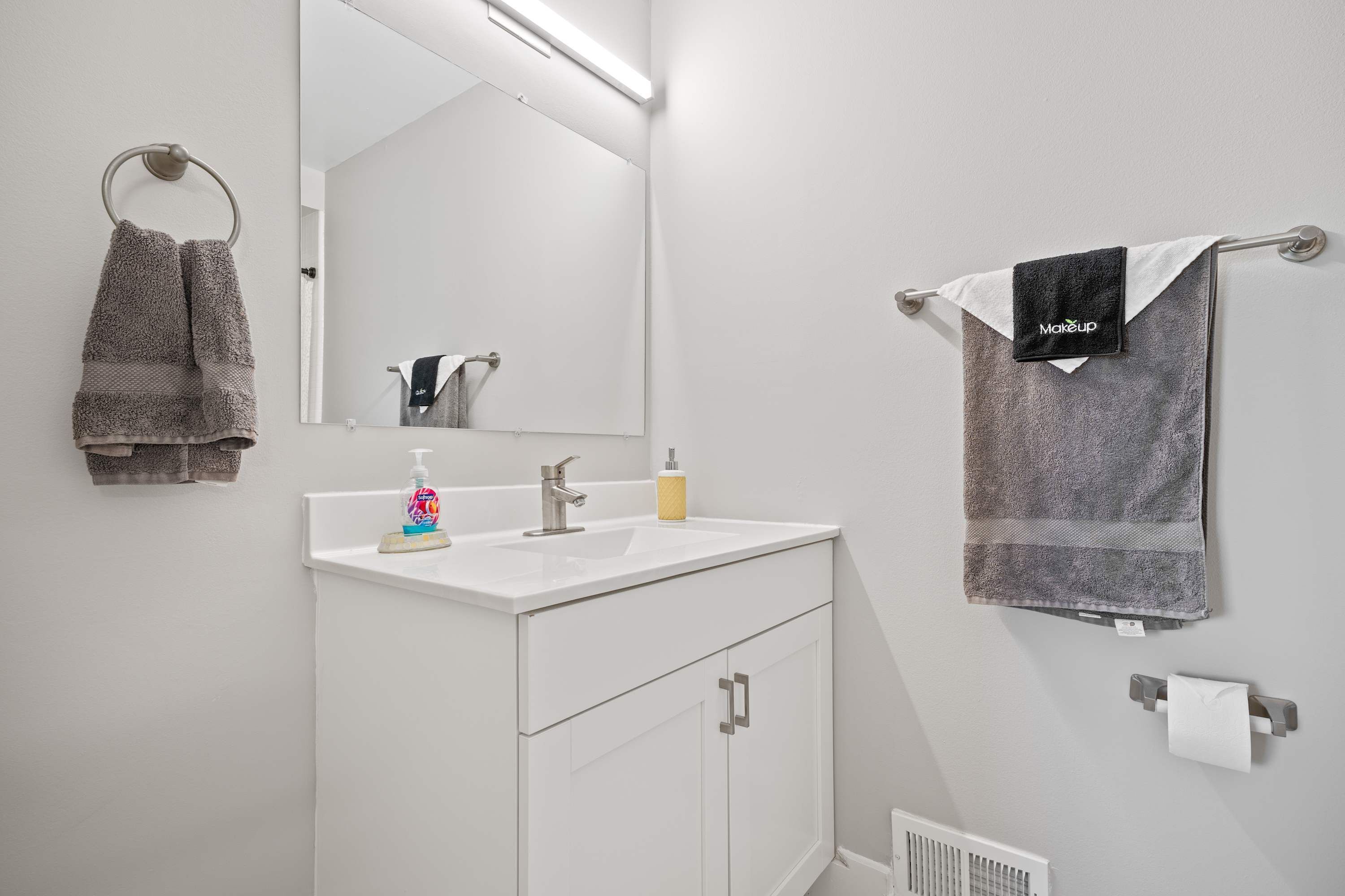 A modern bathroom with a white vanity, a mirror, and two towels hanging on towel rings.