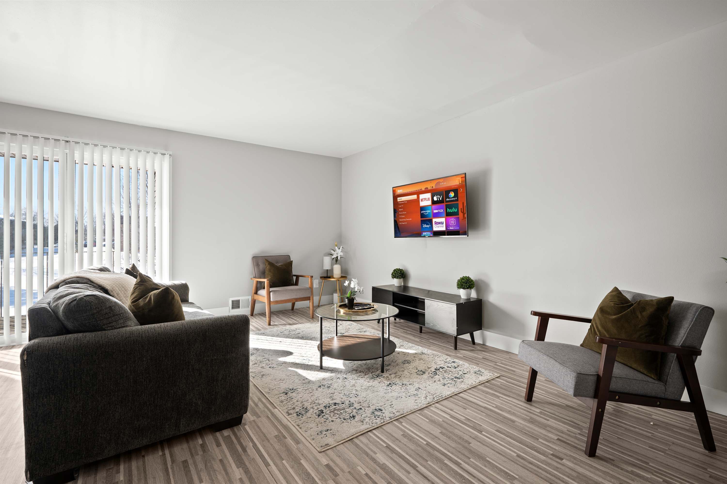A modern living room with a flat-screen TV mounted on the wall, a grey sofa, a round coffee table, and a side table with a plant.
