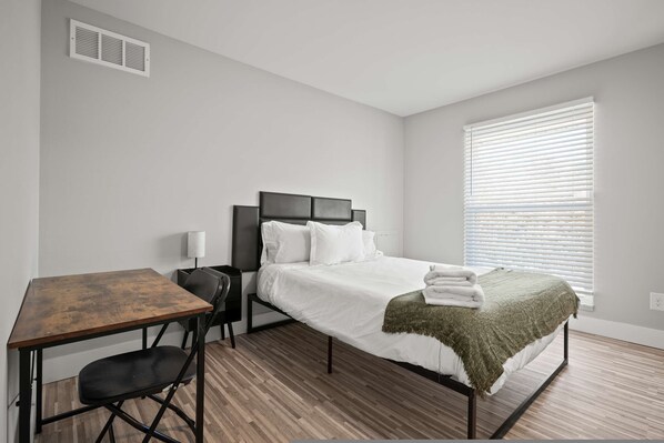 A bedroom with a bed, a desk, a chair, and a window with blinds. - A Unique 2BR 2BA Stay (Rochester)