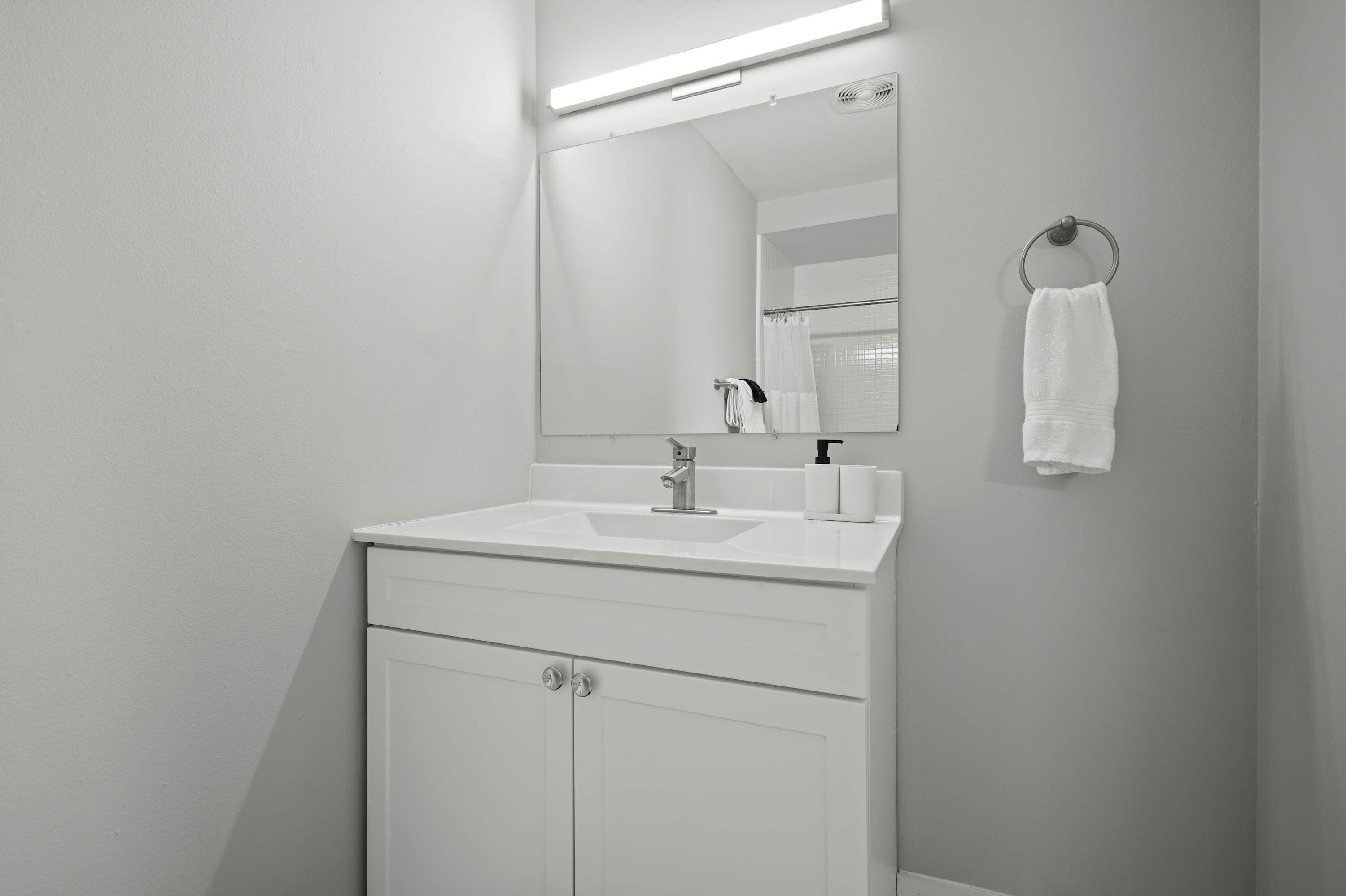 A modern bathroom with a white sink, mirror, and towel ring.