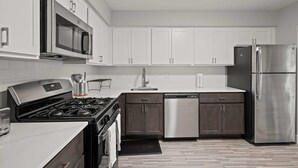 A modern kitchen with white cabinets, stainless steel appliances, and a wooden floor.