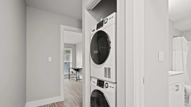 A laundry room with stacked washers and dryers, a shower area, and a hallway leading to another room.