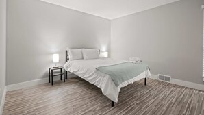 A bedroom with a bed, two bedside tables, a nightstand, a lamp, and a window.
