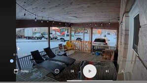 A covered outdoor area with a wooden deck, lounge chairs, and a view of a snowy parking lot with vehicles. - Great Place to Stay When Visiting - Pet Friendly (Rushville)