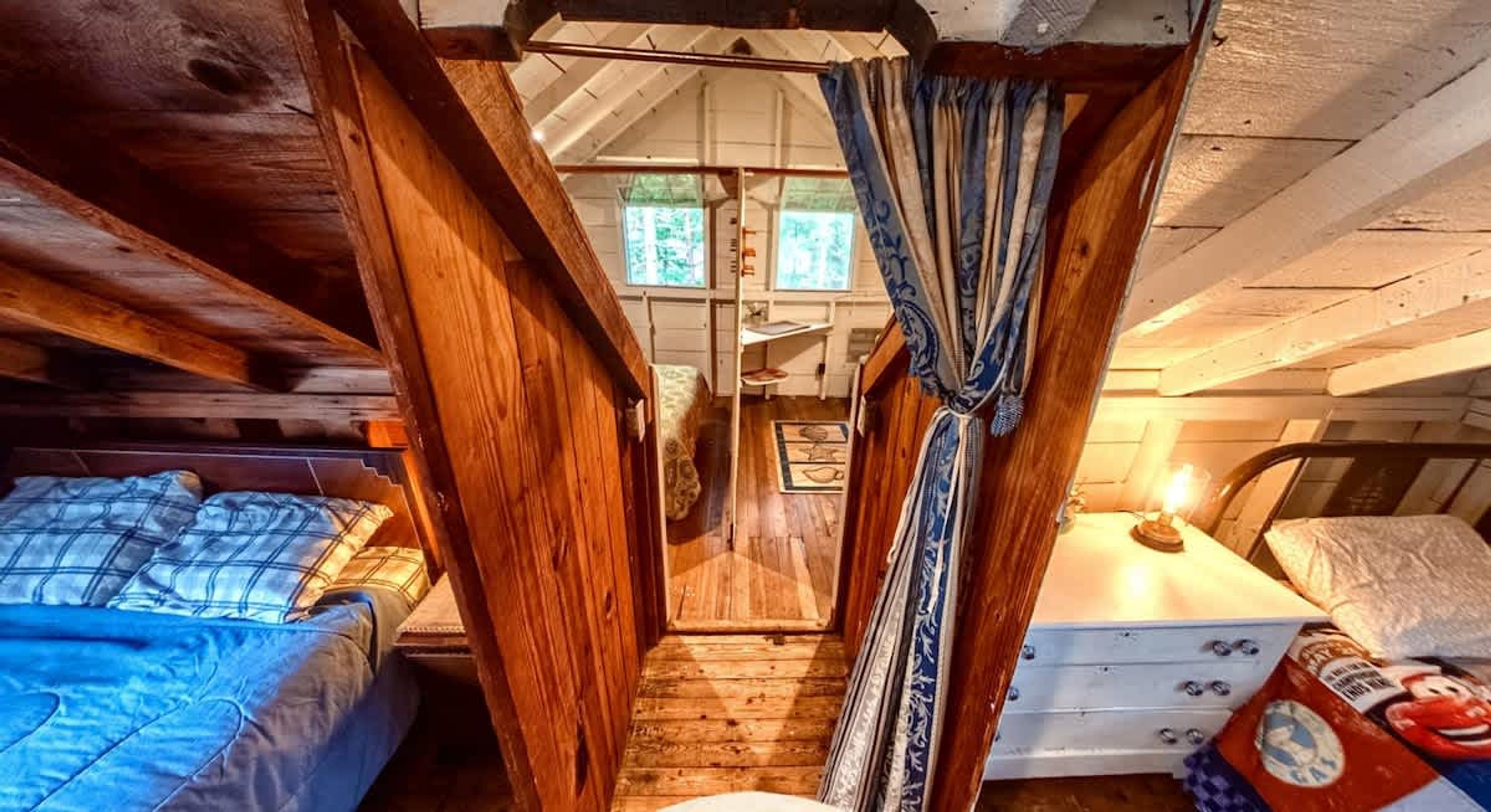 Un dormitorio acogedor en el ático, con vigas de madera, un ventanal pequeño y una cama con manta azul.