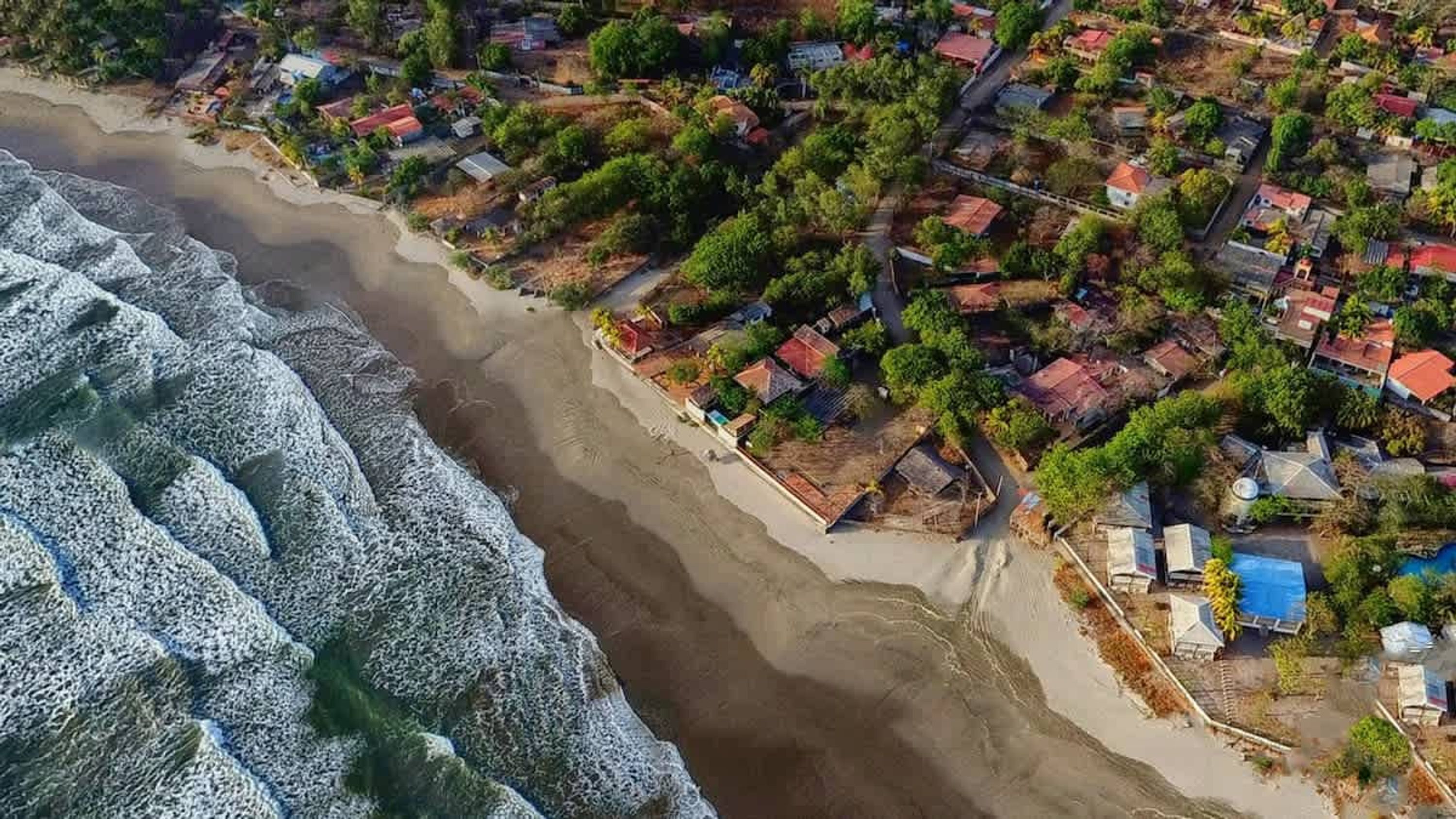 An aerial view of a coastal residential area with houses, a beach, and waves.