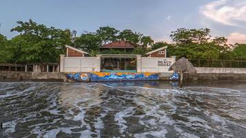 A building labeled "The Beach House" with a thatched roof, situated by a body of water with waves.