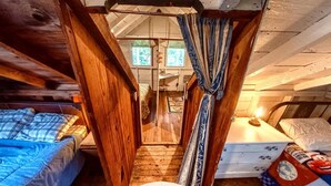 Ein gemütliches Schlafzimmer im Dachgeschoss mit Holzbalken, einem kleinen Fenster und einem Bett mit blauer Decke.