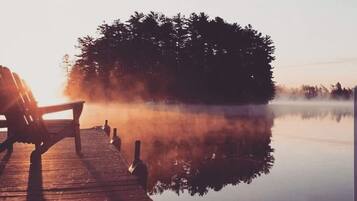 A wooden pier extending into a calm lake with a bench and a bottle, surrounded by trees and mist.