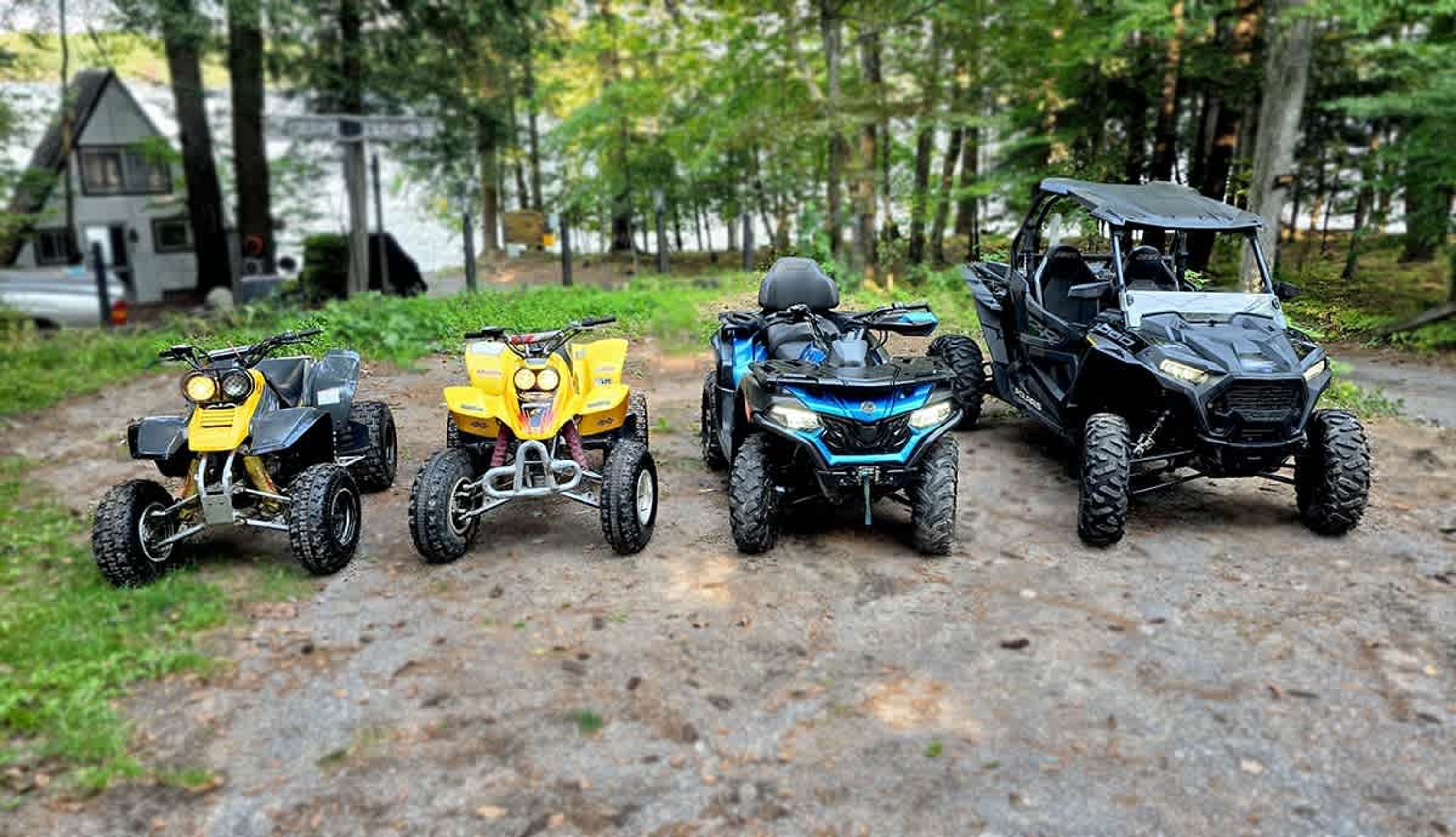 Four off-road vehicles parked on a dirt path in a wooded area.