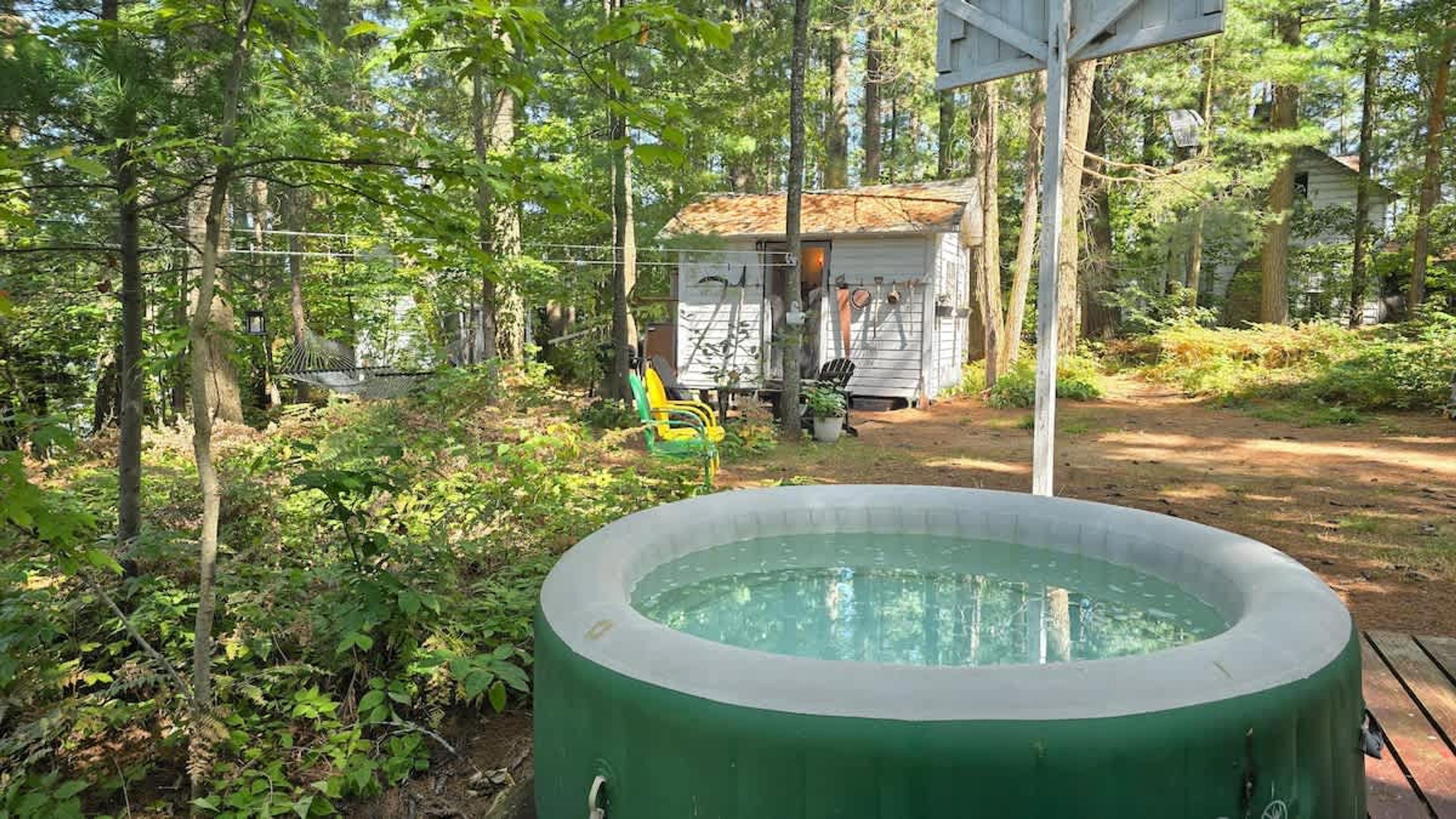 A hot tub in a wooded area with a small cabin in the background.