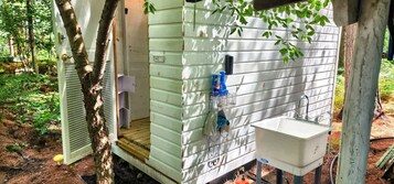 Una cabaña pequeña de una sola habitación con una terraza de madera, una ventana y un lavabo.