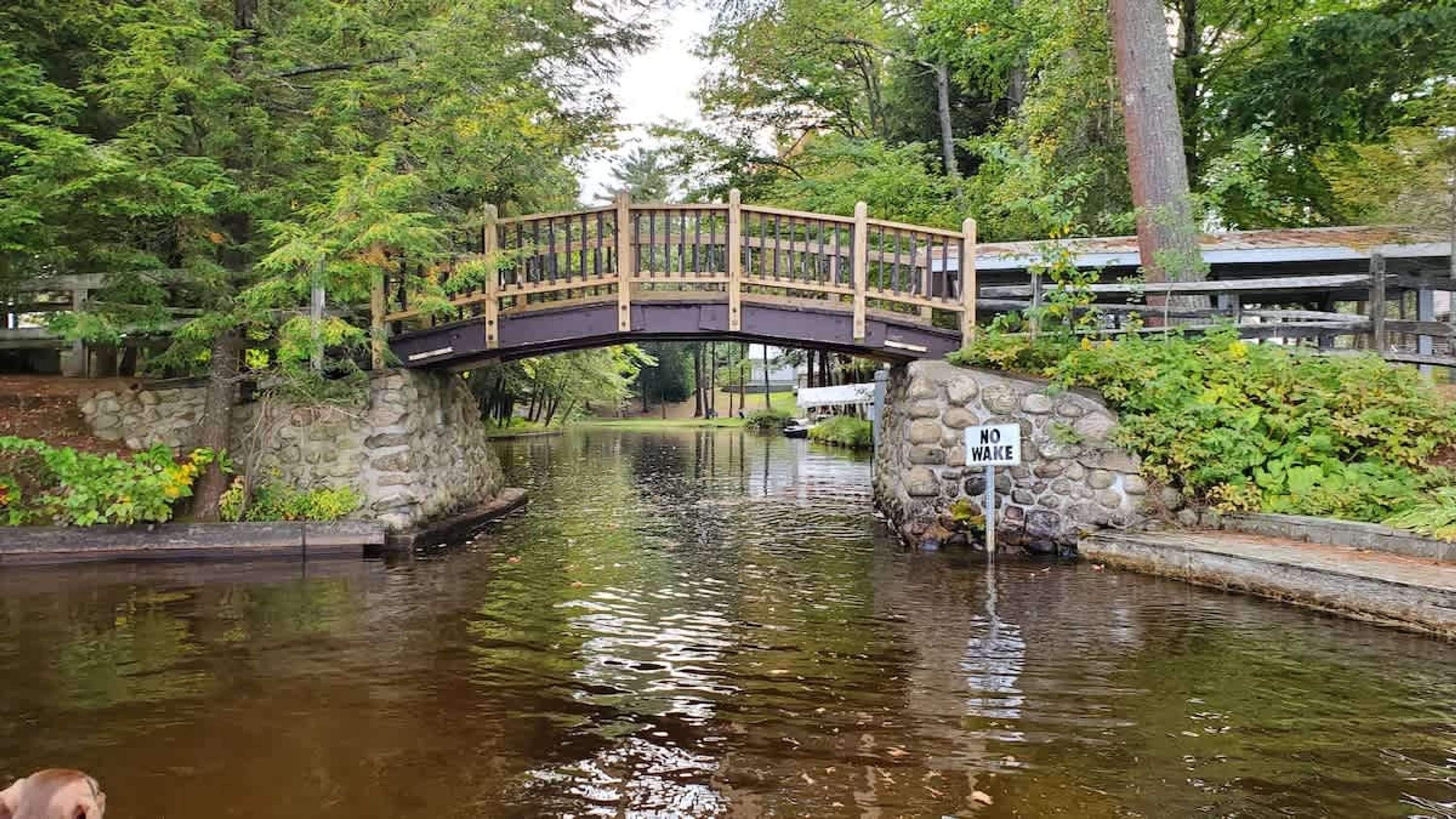 A stone bridge over a canal with a 'NO WAKE' sign, surrounded by greenery.
