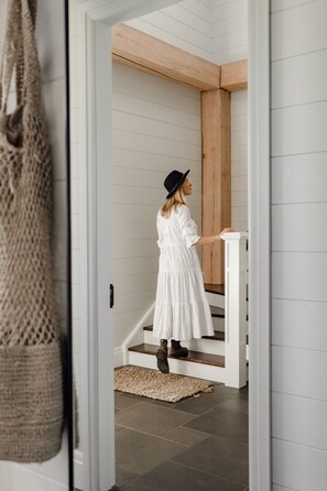 A person in a white dress and hat standing at a white staircase with a wooden ceiling. - The Loft at Linnaeus Farm Berry - by Linnaeus Collection (Berry)