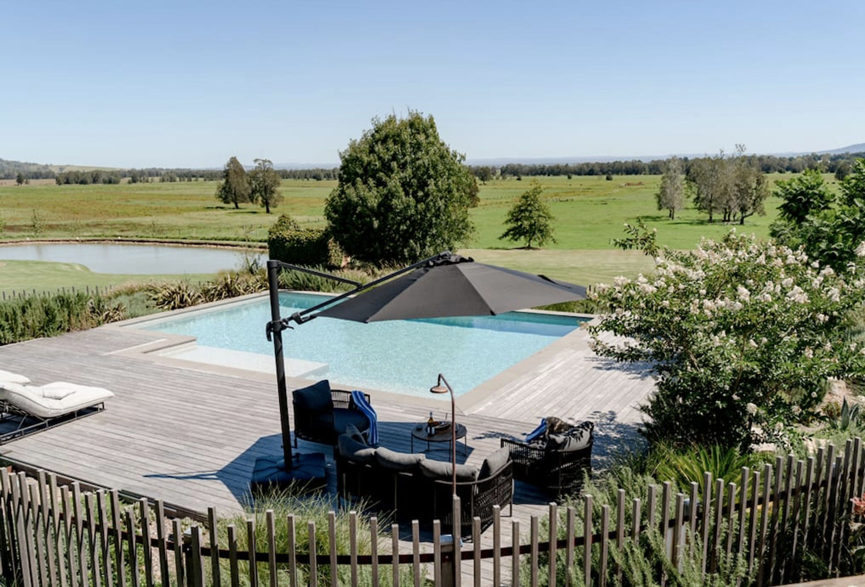 A pool area with a wooden deck, lounge chairs, and a large umbrella.