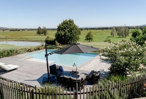 A pool area with a wooden deck, lounge chairs, and a large umbrella. - The Loft at Linnaeus Farm Berry - by Linnaeus Collection (Berry)