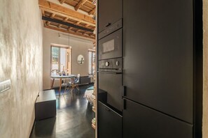 A kitchen with a large black refrigerator, wooden ceiling beams, and a dining area with a table and chairs.