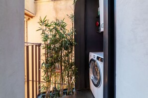 Un espace dédié à la lessive, avec un lave-linge, un bouton rouge et des plantes en bambou.