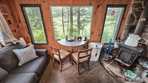 Interior acogedor de una cabaña con chimenea de piedra, una mesa redonda con sillas y un sofá.