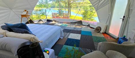 Alojamiento en tienda de campaña con cama, zona de estar y vistas a un lago.