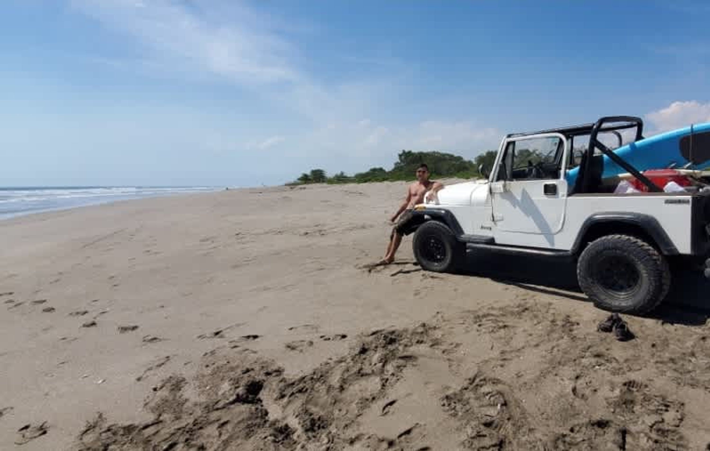 A white vehicle parked on a sandy beach with footprints leading to it.