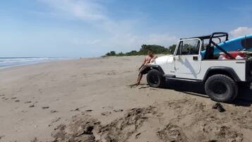 A white vehicle parked on a sandy beach with footprints leading to it.