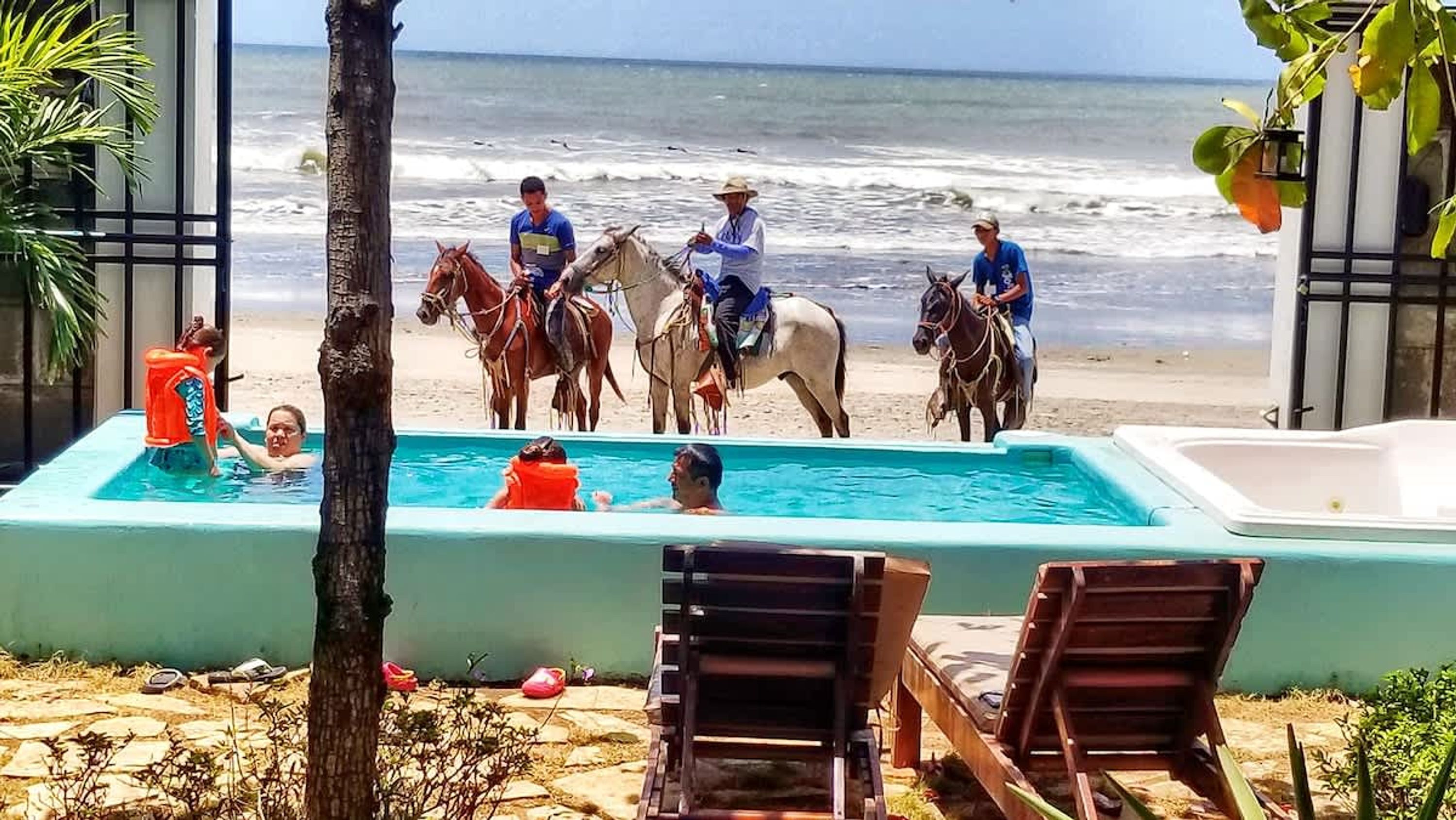 A pool area with people and horses, overlooking the beach and ocean.