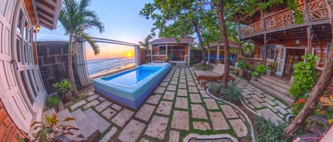 A pool area with a view of the ocean, surrounded by stone pathways and greenery.