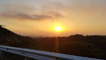 A sunset over a hilly landscape with a metal guardrail in the foreground.