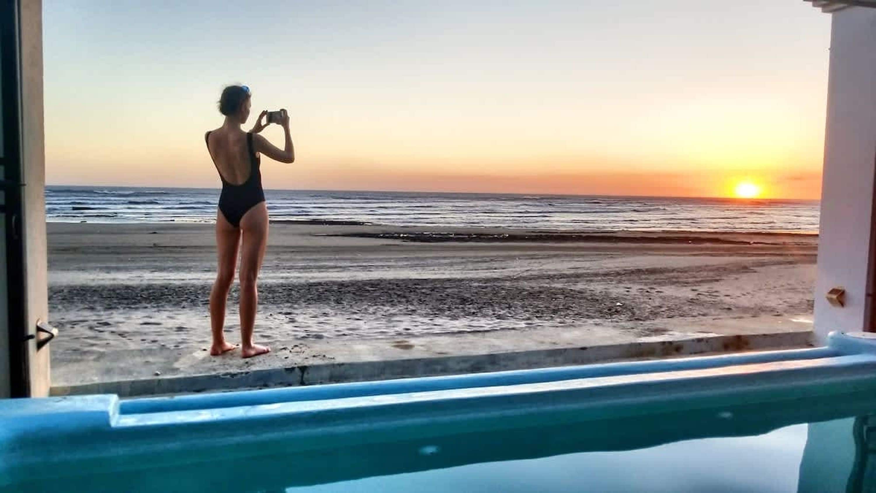 A person taking a photo at a beach during sunset.