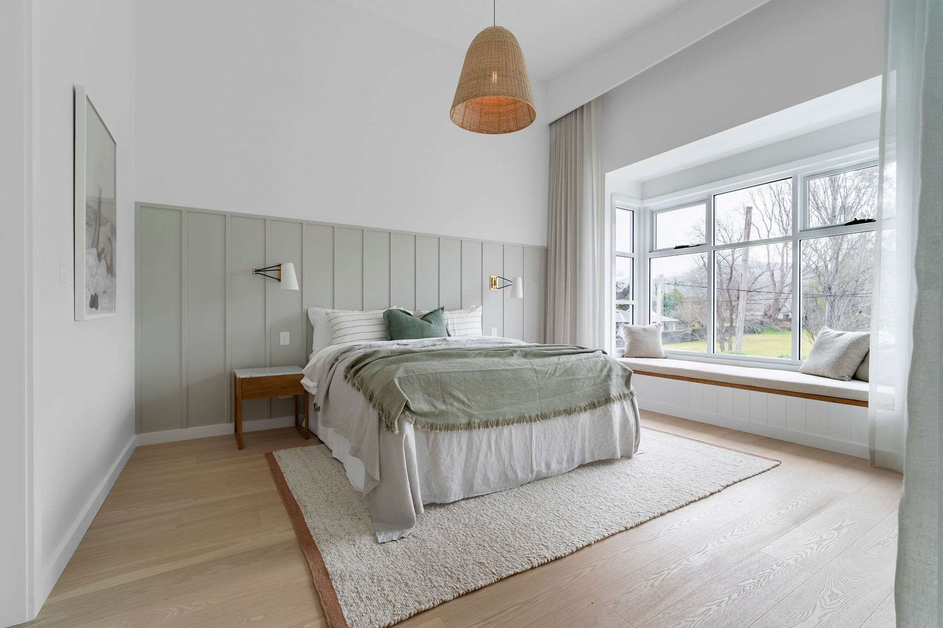 Una camera da letto con un letto, comodini, una panca finestrata e una lampada a sospensione.