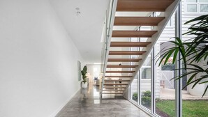 A modern interior with a polished concrete floor, a wooden staircase, and large windows offering a view of the outdoors. - Rubus Pink Berry - by Linnaeus Collection (Berry)