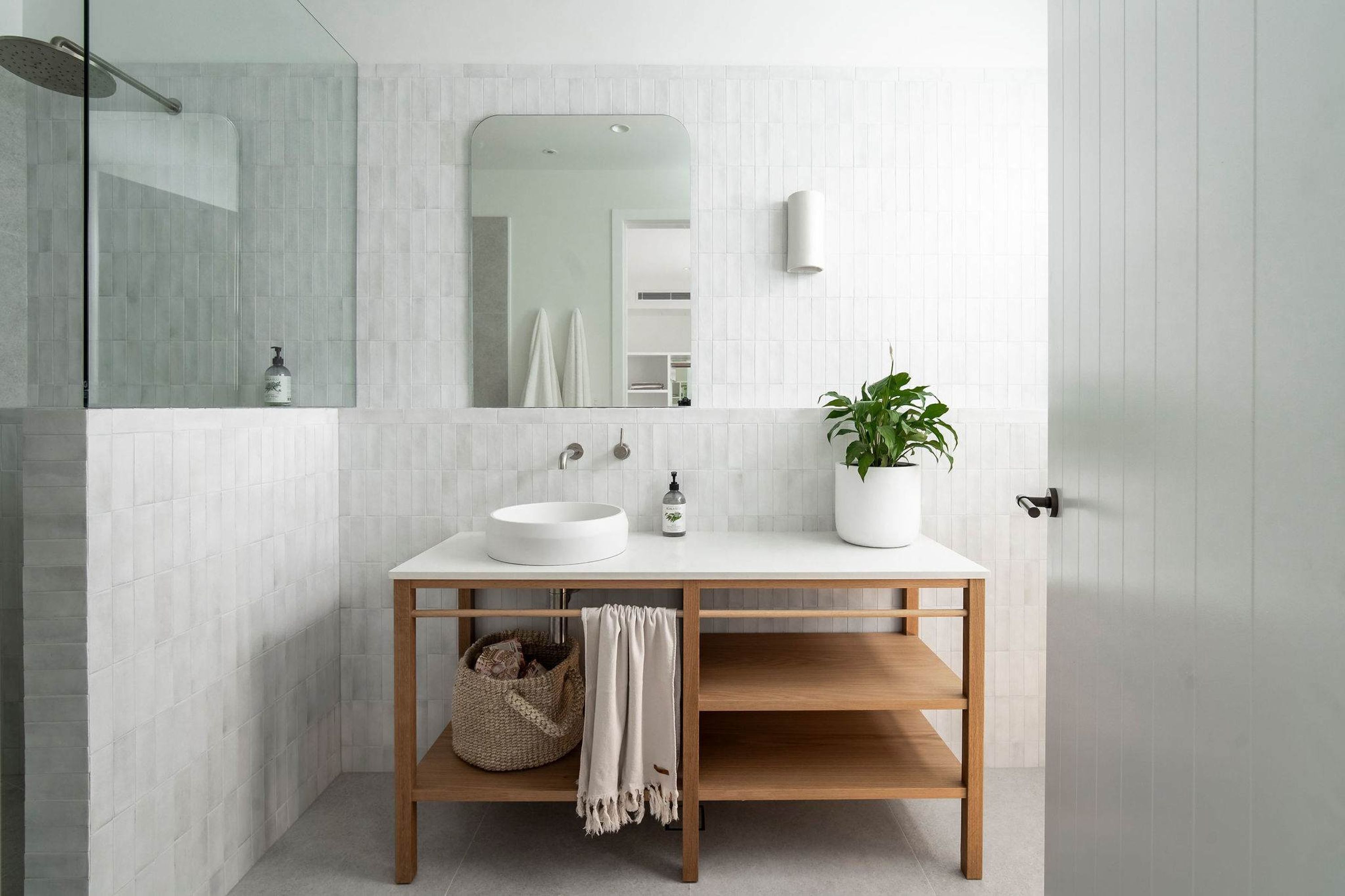 A modern bathroom with a white sink, mirror, and potted plant.