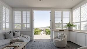 Uma sala de estar acolhedora com um sofá, poltrona e vista para um jardim pelas janelas abertas.