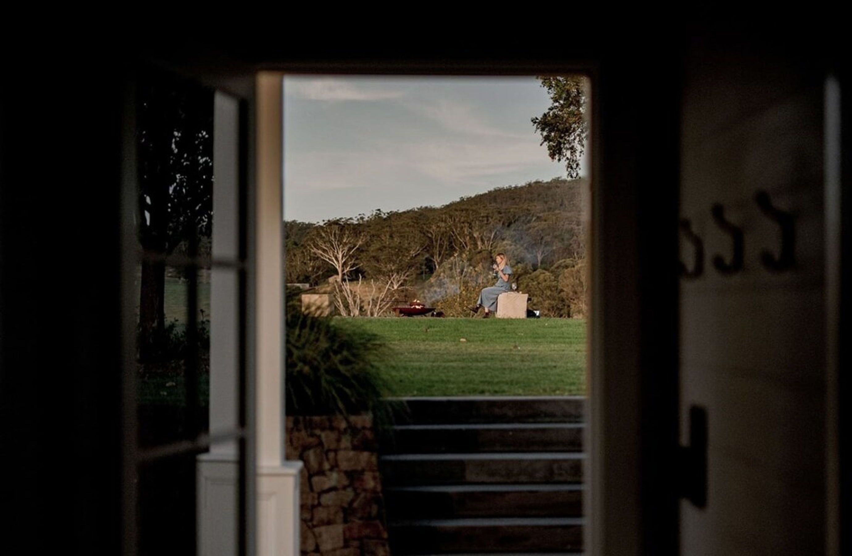 An open doorway leading to a grassy area with trees and a stone wall.