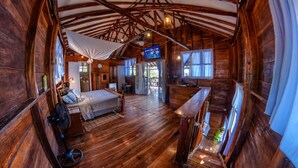A rustic wooden cabin with a bed, a small desk, a TV, and a balcony. - Beachfront 1-of-a-kind House w AC Pool Wifi ATV (San Rafael del Sur)