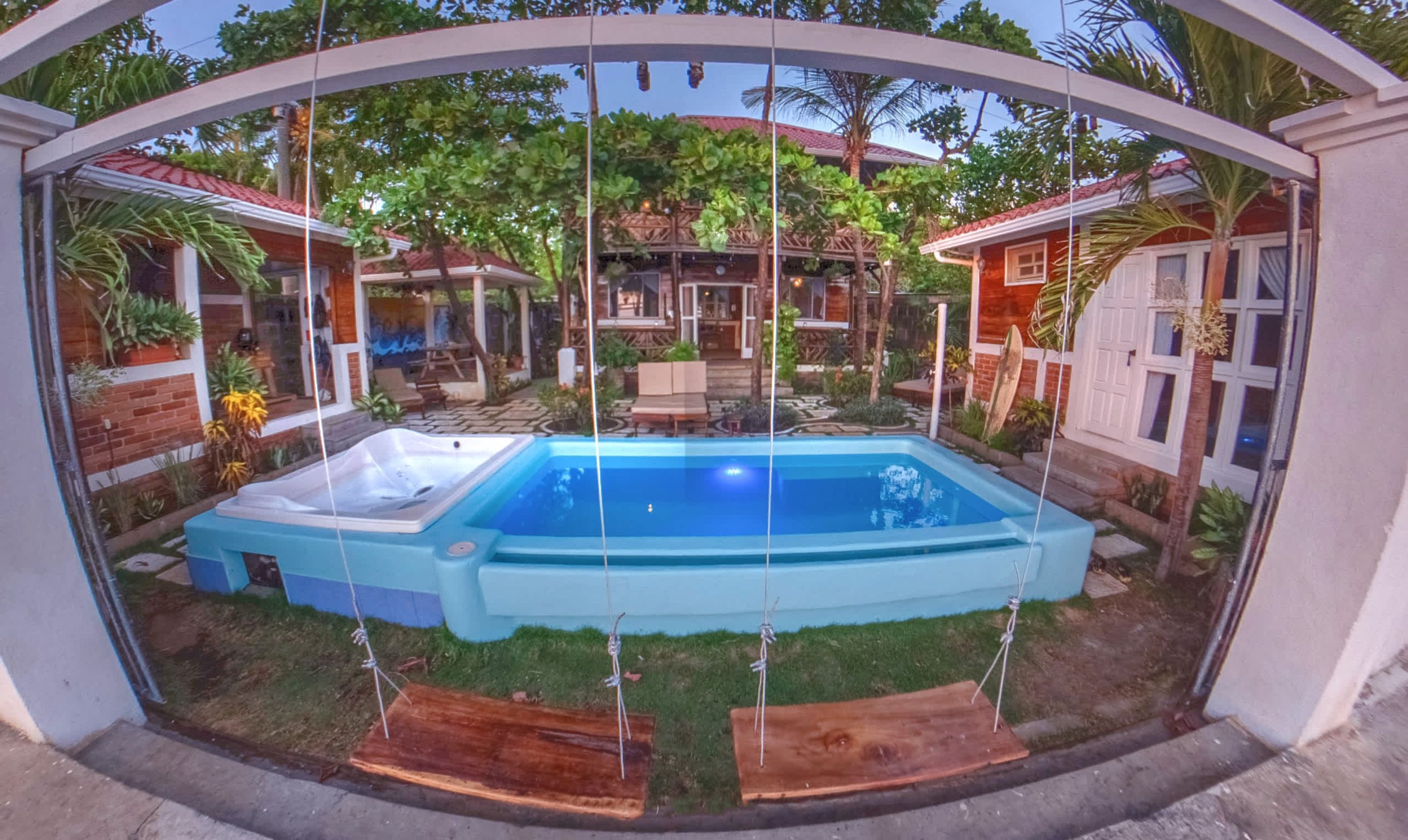 Una piscina con idromassaggio, circondata da un giardino con diverse piante e un pontile in legno.