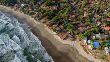 Vue aérienne d’une zone résidentielle côtière, avec des maisons, une plage et des vagues.