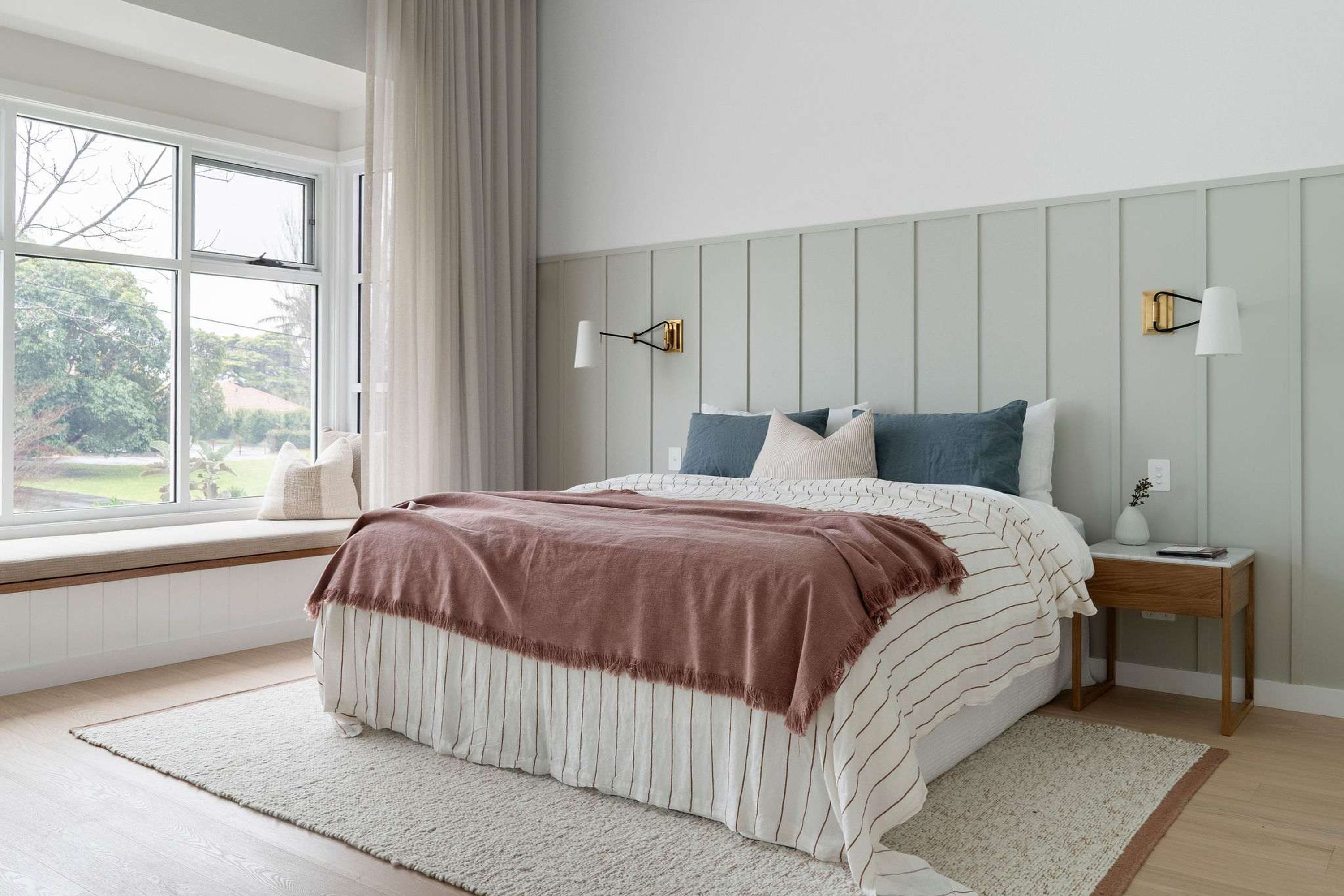 A bedroom with a large window, a bed with striped bedding, two bedside tables, and wall-mounted lamps.