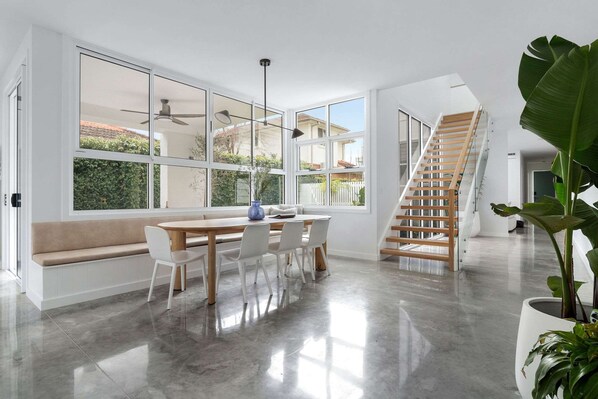 A spacious room with a large window, a wooden staircase, a dining area with a bench, and a potted plant.