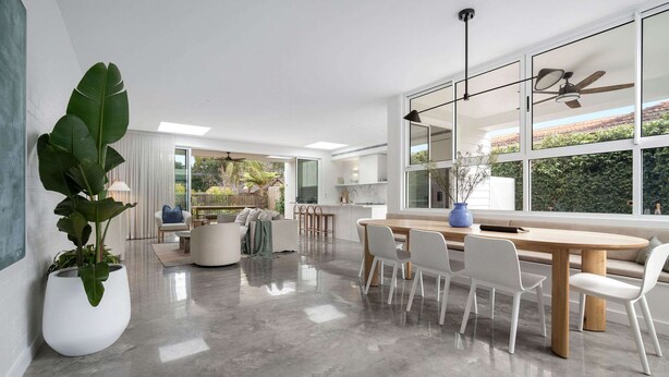 A modern dining area with a wooden table and white chairs, large windows with a view of greenery, and a ceiling fan. - Rubus Green Berry - by Linnaeus Collection (Berry)