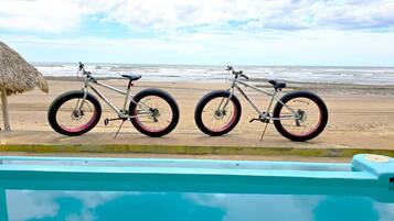 Two bicycles parked by a poolside with a beach and ocean in the background.