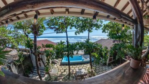 A view through a wooden archway overlooking a pool area with a clear ocean view. - Balcony Bedroom Suite w Romantic Sunsets - AC - Pool (San Rafael del Sur)